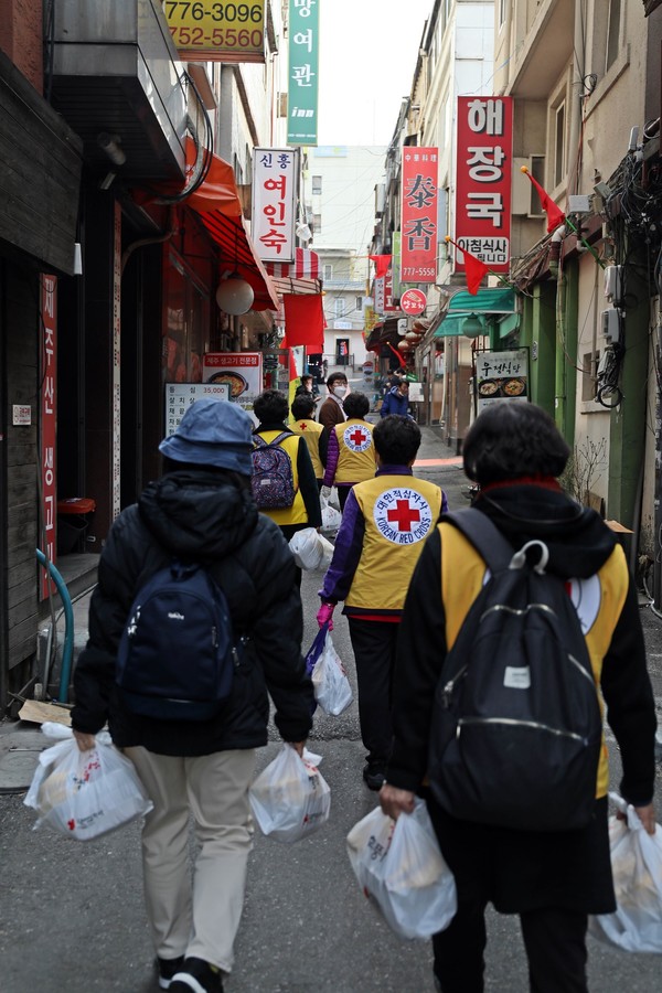 사진: 적십자 봉사원들이 9일(화) 서울 용산구 후암동 일대에서 쪽방촌 거주민에게 밑반찬을 전달하기 위해 이동하고 있다. 대한적십자사는 매주 화요일마다 취약계층 200가구를 대상으로 1주일치 밑반찬을 제작해 전달하는 ‘1004가 전해주는 황금도시락 사업’을 전개한다.