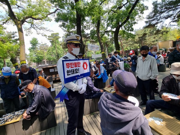 강북경찰서 경찰관이 어르신들이 많이 이용하는 공원에서 무단횡단 안되요 라는 팻말을 들고 있다.